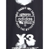 Close-up of Y-3 T-Shirt maxi print with Adidas logo and text in white. High-contrast graphic detail on premium black men's T-shirt.