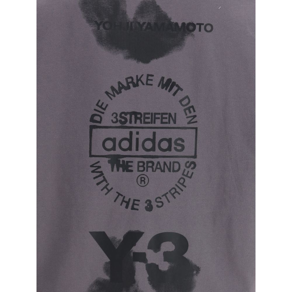 Close-up of Y-3 T-Shirt with maxi print highlighting Adidas logo, Yohji Yamamoto text, and artistic black graphic details on gray fabric.